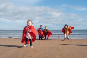 University Nursery children in specially made red gowns enjoy a playdate at St Andrews East Sands